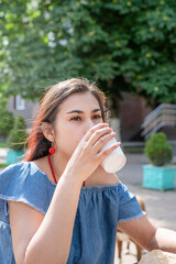 Stylish millennial woman drinking coffee at street cafe in summer