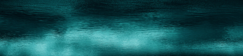 Blue green water surface. Night. Small waves. Ripples. Reflection of light. Dark teal water background with space for design. Web banner. Wide. Panoramic.