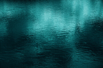 Blue green water surface. Night. Small waves. Ripples. Reflection of light. Dark teal water...