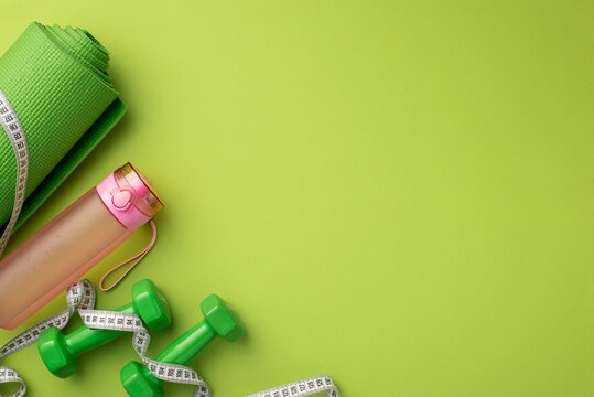 Slimming concept. Top view photo of sports mat tape measure pink bottle of water and dumbbells on isolated green background with empty space