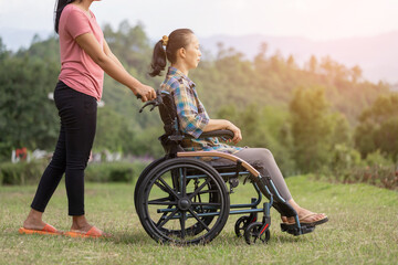 person sitting in wheelchair with care helper walking on mountain meadow park in sunny day.