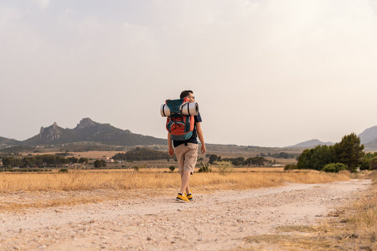 Aventurero caminando en un camino entre prados, con la mochila con esterilla. Fotograf&iacute;a horizontal con espacio para texto.