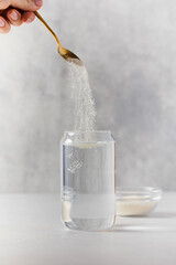 Hydrolyzed collagen powder is added with a spoon to a transparent glass of water on a grey...