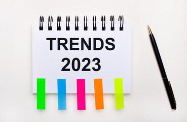 On a light background, a pen, a notebook with the text TRENDS 2023 and bright stickers.