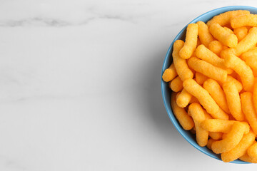 Bowl of tasty cheesy corn puffs on white marble table, top view. Space for text