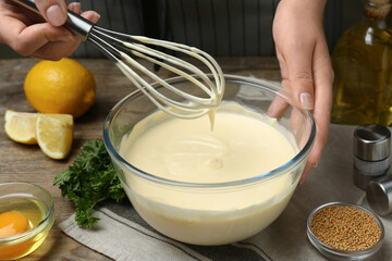 Woman making homemade mayonnaise in glass bowl at wooden table, closeup