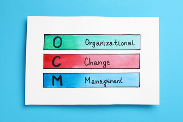 Paper with OCM abbreviation and its interpretation (Organizational Change Management) on light blue background, top view