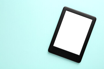 Modern e-book reader with blank screen on light blue background, top view. Space for text