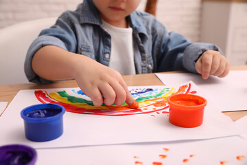 Little child painting with finger at wooden table indoors, closeup
