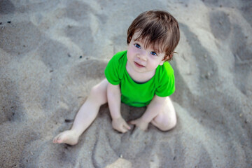 Little child sitting on the sandy beach and looking up in Poland