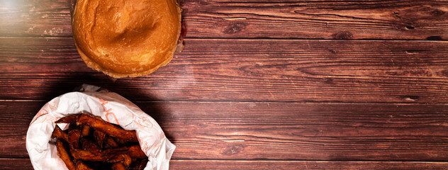 Top view of a hamburger with french fries on a dark wood table. Beef burger. Horizontal banner with space for text. 