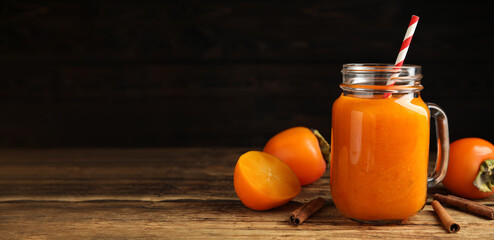 Tasty persimmon smoothie with cinnamon on wooden table against dark background, space for text. Banner design