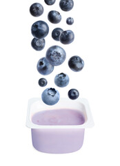 Many fresh blueberries falling into plastic cup with yogurt on white background