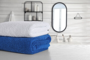 Stacked clean towels on white wooden table in bathroom. Space for text