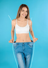 Happy young woman with slim body in oversized jeans on light blue background. Weight loss