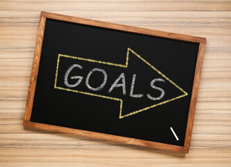 Obraz premium Blackboard with drawn arrow and word GOALS on wooden background, top view