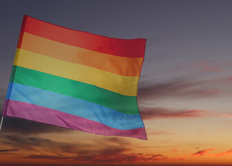 Bright rainbow LGBT flag against sky at sunset