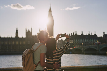 Rearview shot of a couple taking photos of Big Ben with a smartphone while exploring the city of...