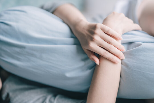 A woman lazily embraces a bolster on the bed, choosing to focus on her hand.