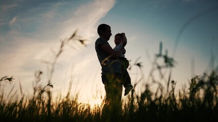 Naklejka na ściany i meble father and son silhouette. happy family kid dream concept. father holding in his arms in the grass in nature at sunset shadow silhouette. fathers day. father and son in the park silhouette sunset