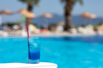 Fototapeta na wymiar Blue lagoon cocktail with ice near swimming pool in sunny day. Summer soft drinks.