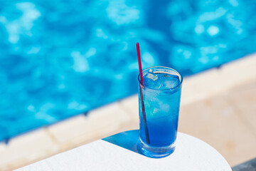 Blue lagoon cocktail with ice near swimming pool in sunny day. Summer soft drinks.