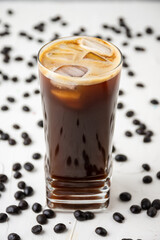 closeup of glass of iced coffee on white table with coffee beans, selective focus, vertical