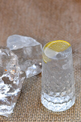 transparent alcoholic cocktail with ice, decorated with a slice of lemon, vertical photo