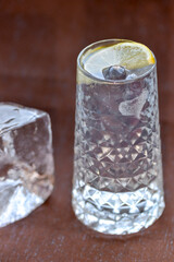transparent alcoholic cocktail with ice decorated with a slice of lemon on a dark background