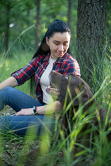 a young caucasian woman in a red plaid shirt plays with an old labrador dog in a green park