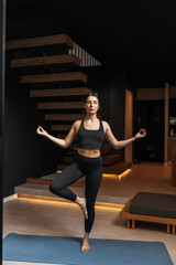 Young caucasian girl with closed eyes develops inner balance standing in tree pose. Brunette woman...