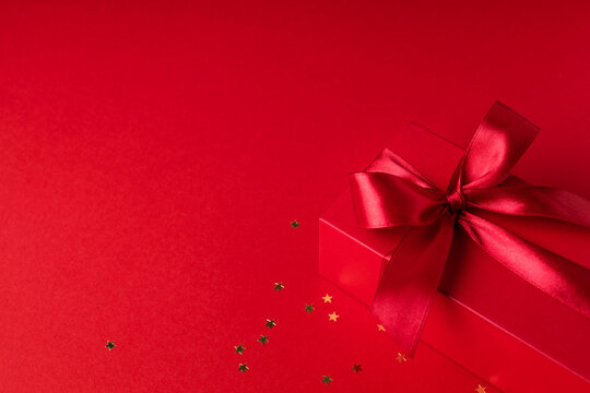 Red gift box for Christmas or Valentine's day on red background with confetti.