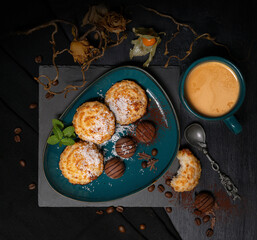 coconut cookies with chocolates on a dark blue-green dish with a cup of coffee with milk on a black background