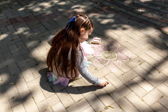 Little preschool girl painting with colorful chalks. Creative outdoors children activity in summer