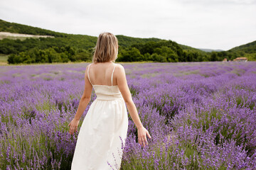 Fototapeta na wymiar Happy young woman in white dress on blooming fragrant lavender fields with endless rows. Bushes of lavender purple aromatic flowers on lavender fields