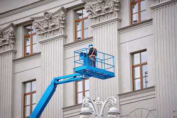 Construction worker in lift bucket of crane restore and repair historic facade of building. Man in...