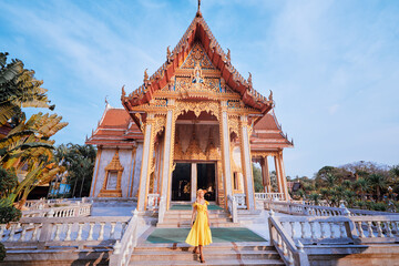 Fototapeta premium Travel by Asia . Young woman in hat and yellow dress walking near the Chalong buddhist temple on Phuket Island in Thailand.