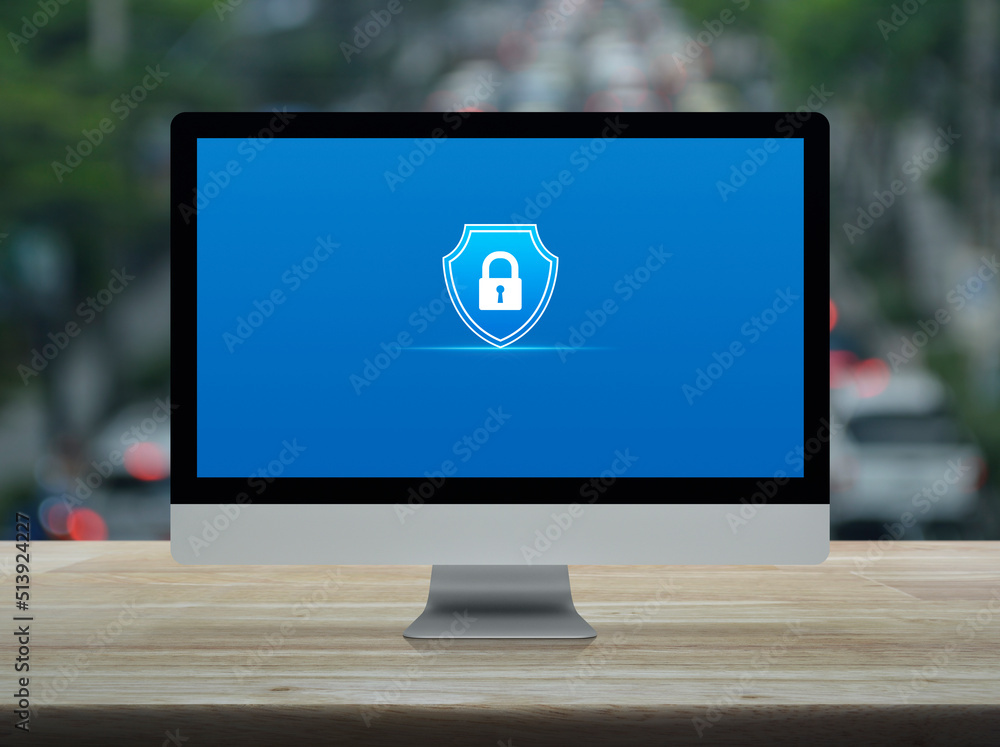 Aufkleber padlock with shield flat icon on desktop modern computer monitor screen on wooden table over blur of
