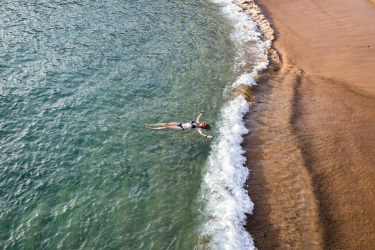 top view of woman floating in the sea near sandy beach