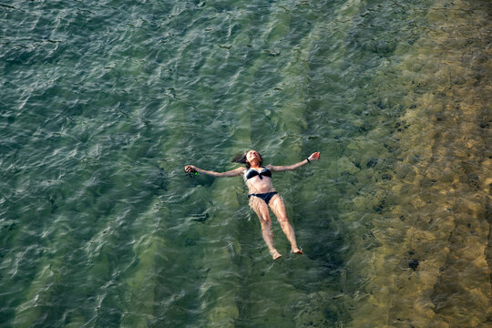 top view of woman floating in the sea near sandy beach