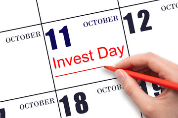 Hand drawing red line and writing the text Invest Day on calendar date October 11. Business and financial concept.