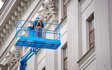 Construction worker in lift bucket of crane restore and repair historic facade of building. Man in...
