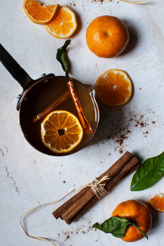Apple cider heated in a copper pot, with oranges with leaves, orange slices, and cinnamon sticks