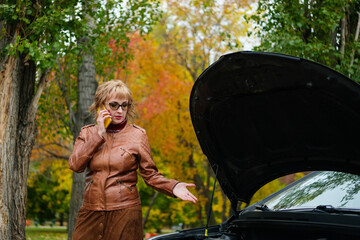 Woman with glasses near a broken car on the road is calling on mobile phone in service, insurance...