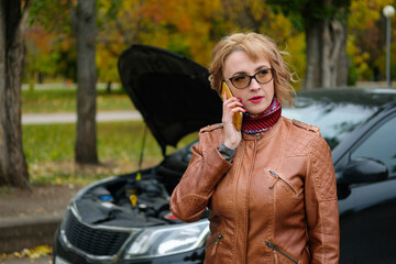 Woman with glasses near a broken car on the road is calling on mobile phone in service, insurance company, tow truck.
