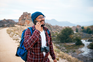 Naklejka premium A young backpacker laughs on a call in the mountains while hiking in autumn
