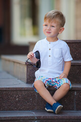 blond boy in a white shirt and shorts holds glasses