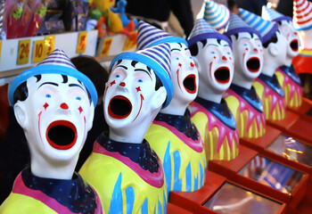 A row of colourful toy clowns with open mouths, an attraction at a fair, close up