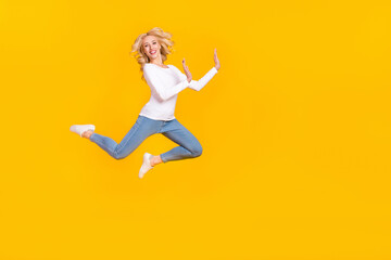 Fototapeta na wymiar Full size photo of pretty millennial blond lady jump wear shirt jeans shoes isolated on yellow background