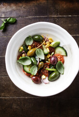 Simple Salad with Green and Kalamata Olives, Cucumber, Cherry and marinated Tomatoes, Capers and Jalapeno Pepper. Brown wooden background. Top view.